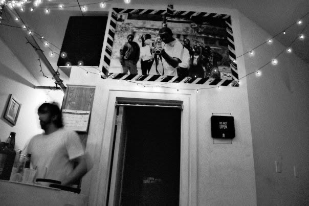 A blurred figure moving beneath string lights and a large photograph in a small room