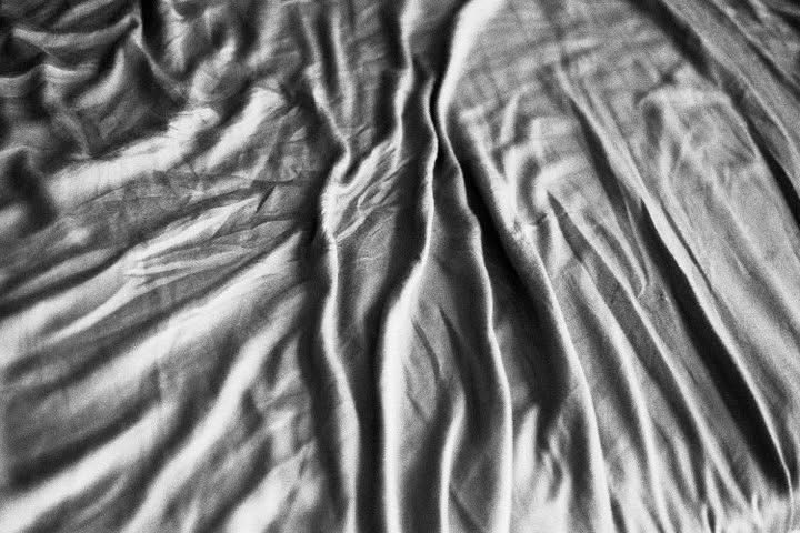 Light and shadow folding across rumpled bed linen in black and white