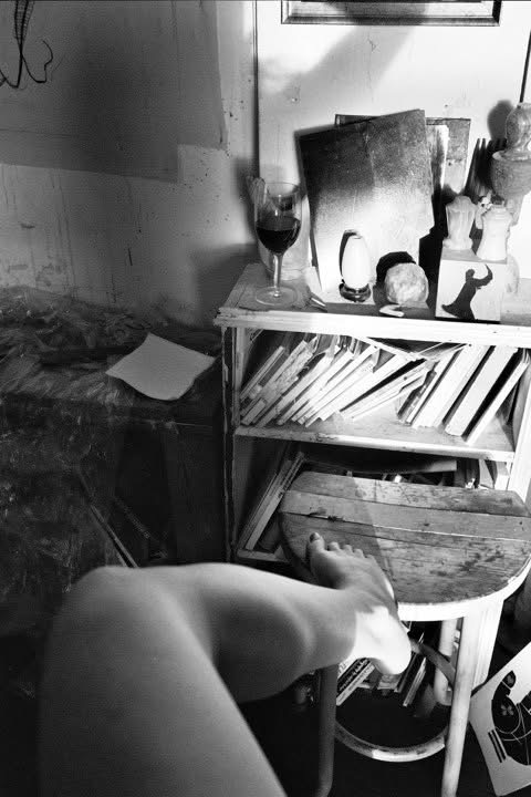 Bare legs and feet extending into a room of books, mirrors, and small objects