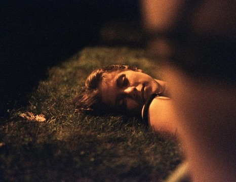 A woman lying on grass at night in warm low light, partly obscured by the foreground