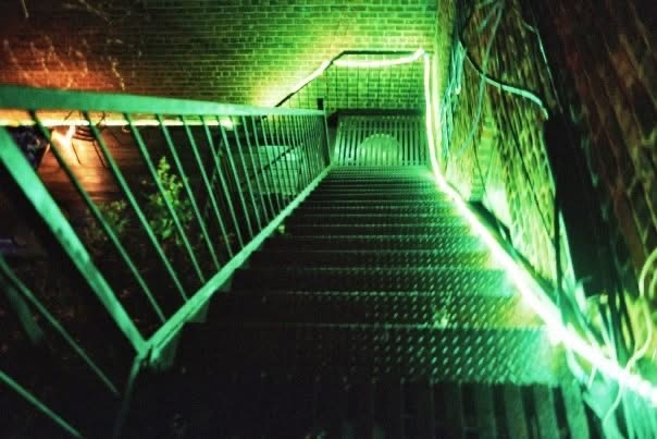 A steep exterior stairwell illuminated by vivid green light at night