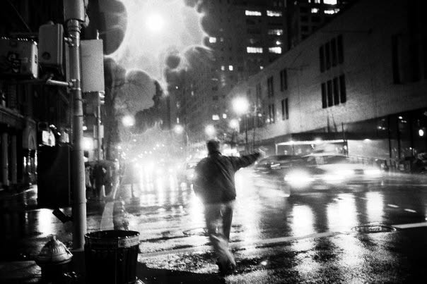 A solitary figure crossing a rain-darkened New York street at night