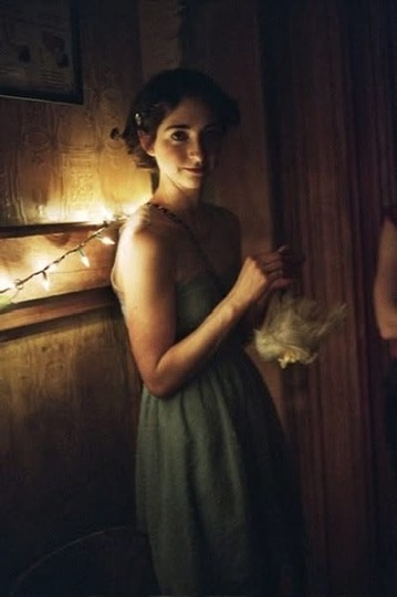 A woman in a dark dress standing beside string lights in a dim wood-paneled room