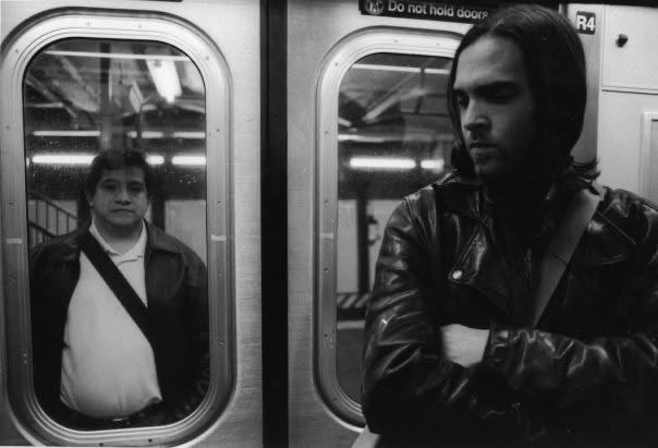 Two subway passengers divided by a pair of train doors