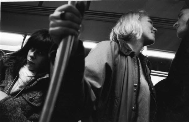 Subway passengers seen from a low angle around a vertical pole