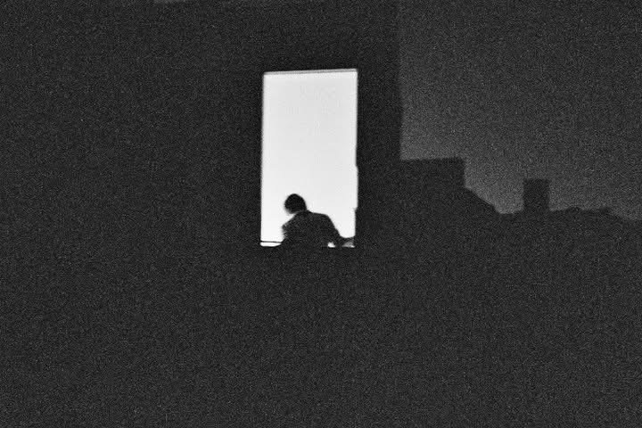 A solitary figure silhouetted in a bright rectangular window at night