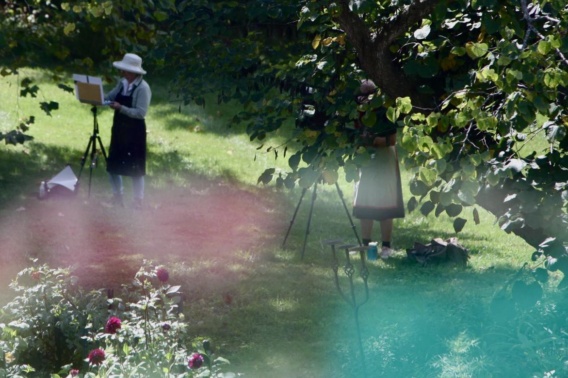 Two painters working at easels beneath the shade of a tree