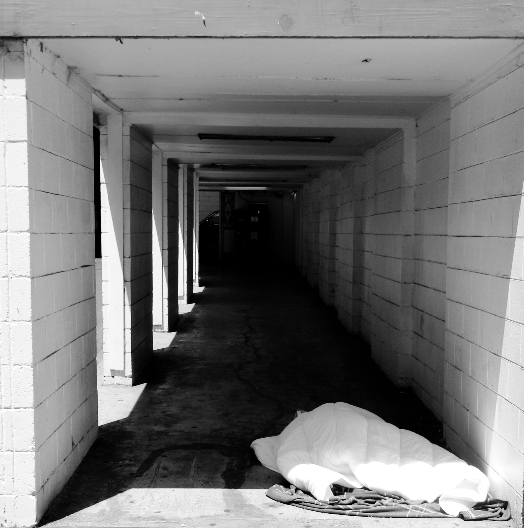 A sleeping place arranged beneath a concrete passageway, photographed in black and white