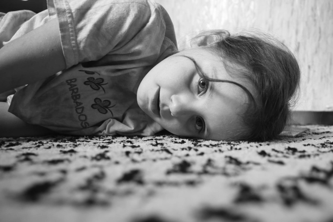 A child lying on a patterned carpet and looking toward the camera