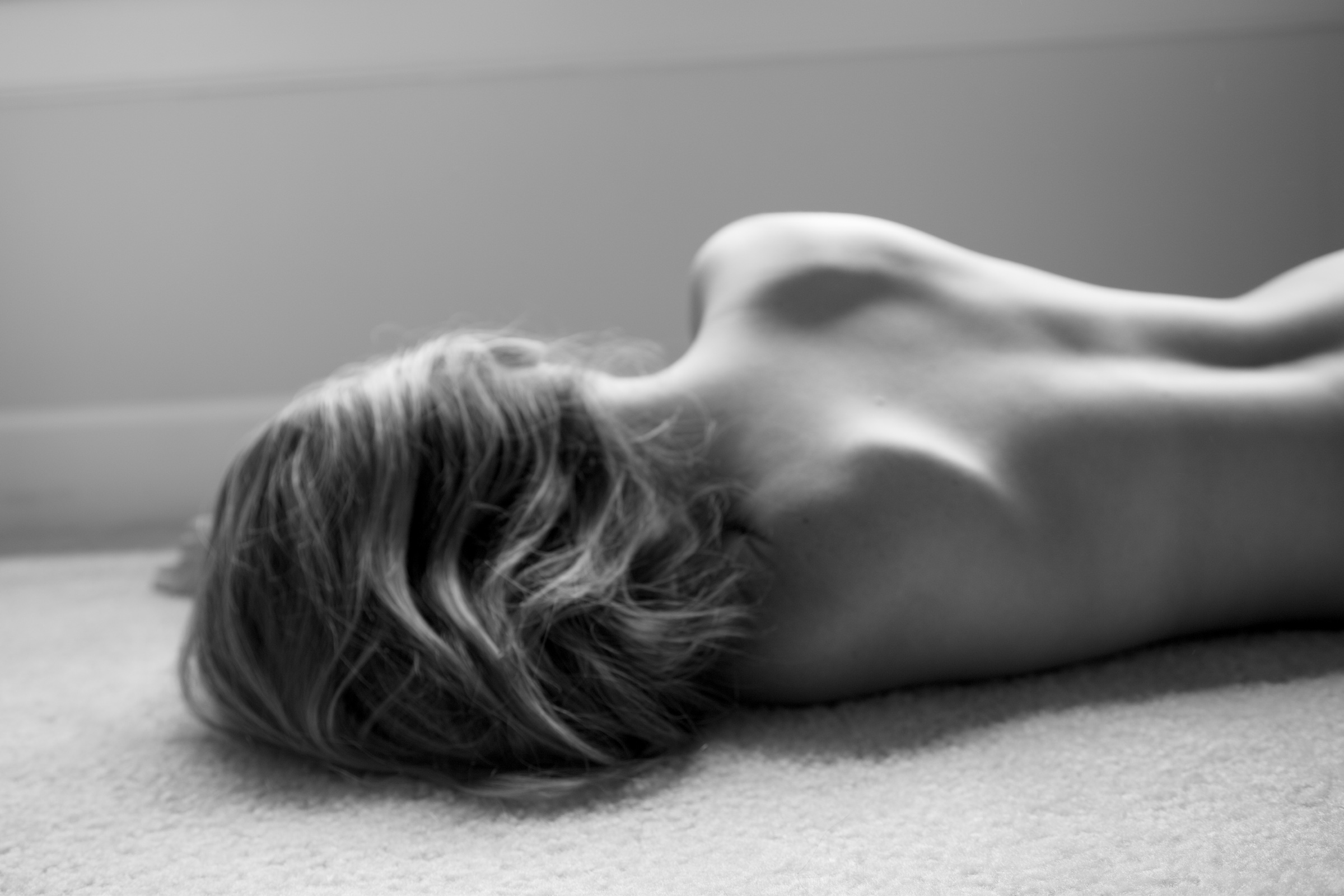 A child lying on a carpet, her back traced by soft window light, in black and white
