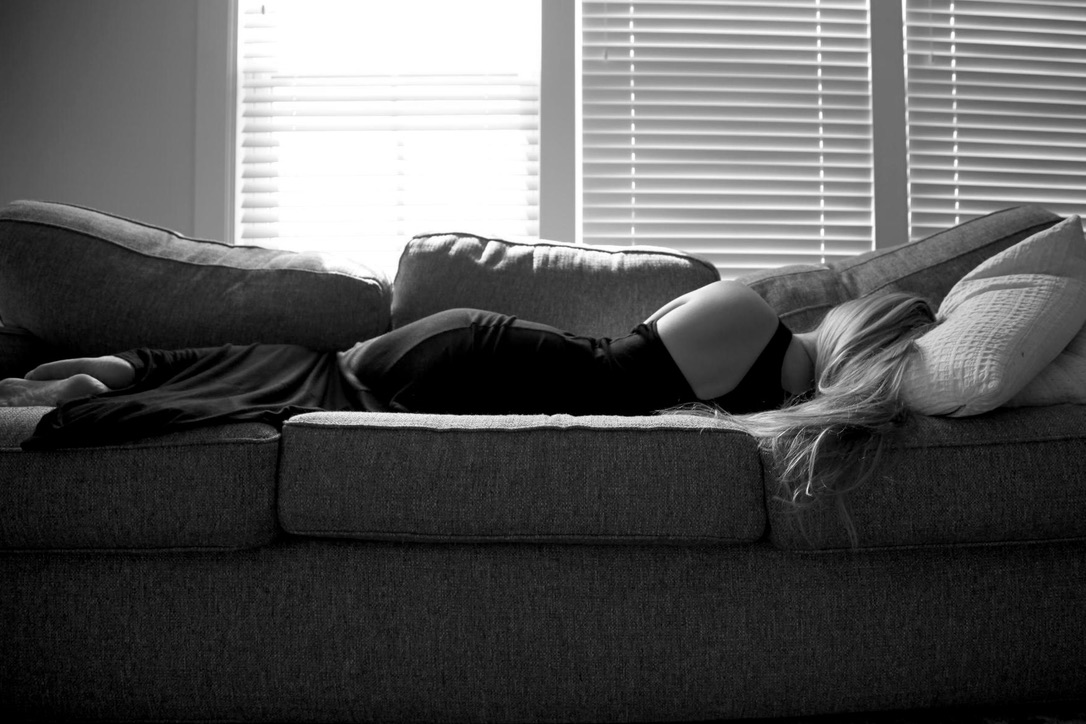 A woman lying across a couch before bright windows in black and white