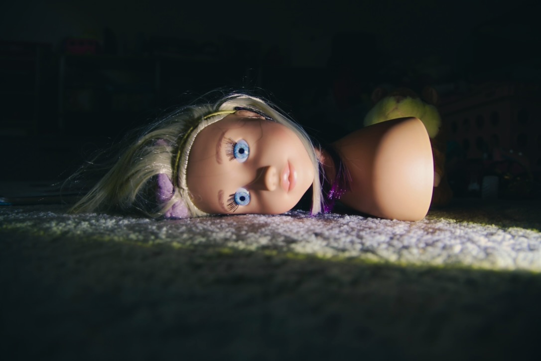 A blonde doll lying in a narrow band of sunlight on a dark carpet
