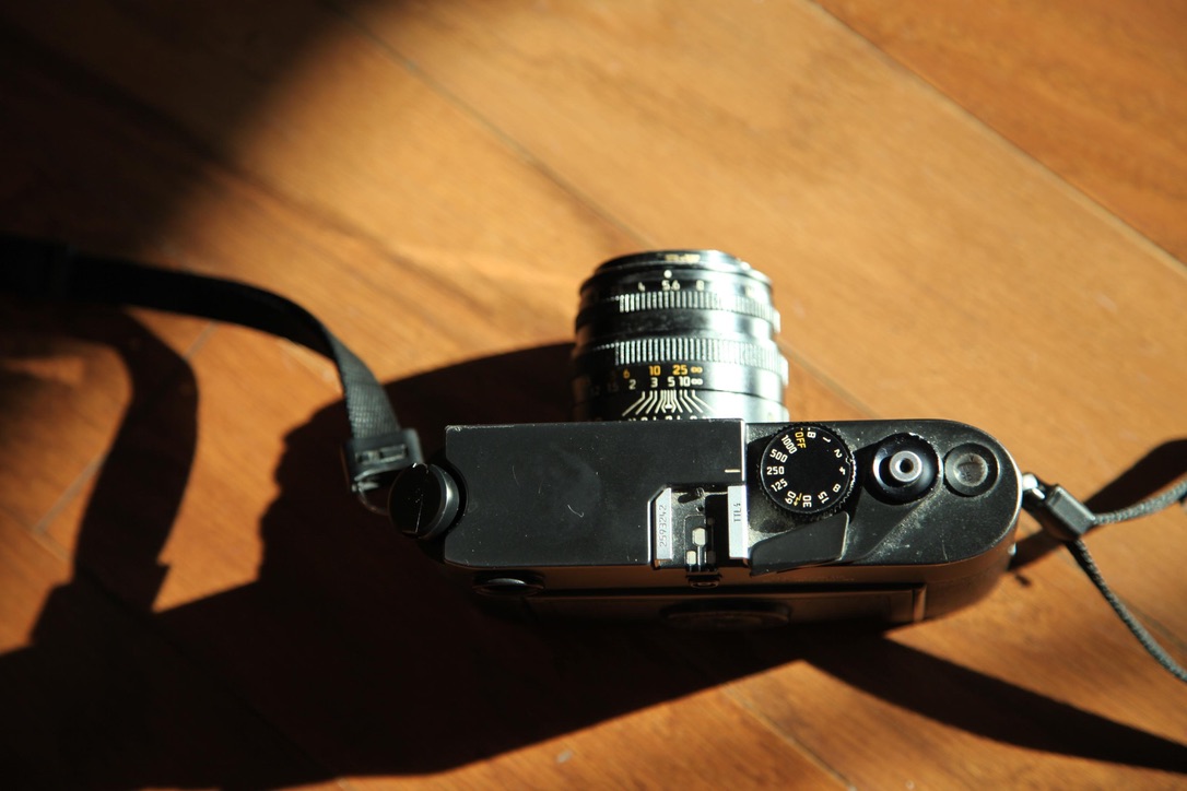 A worn Leica M6 camera seen from above in warm sunlight, its strap casting a long shadow