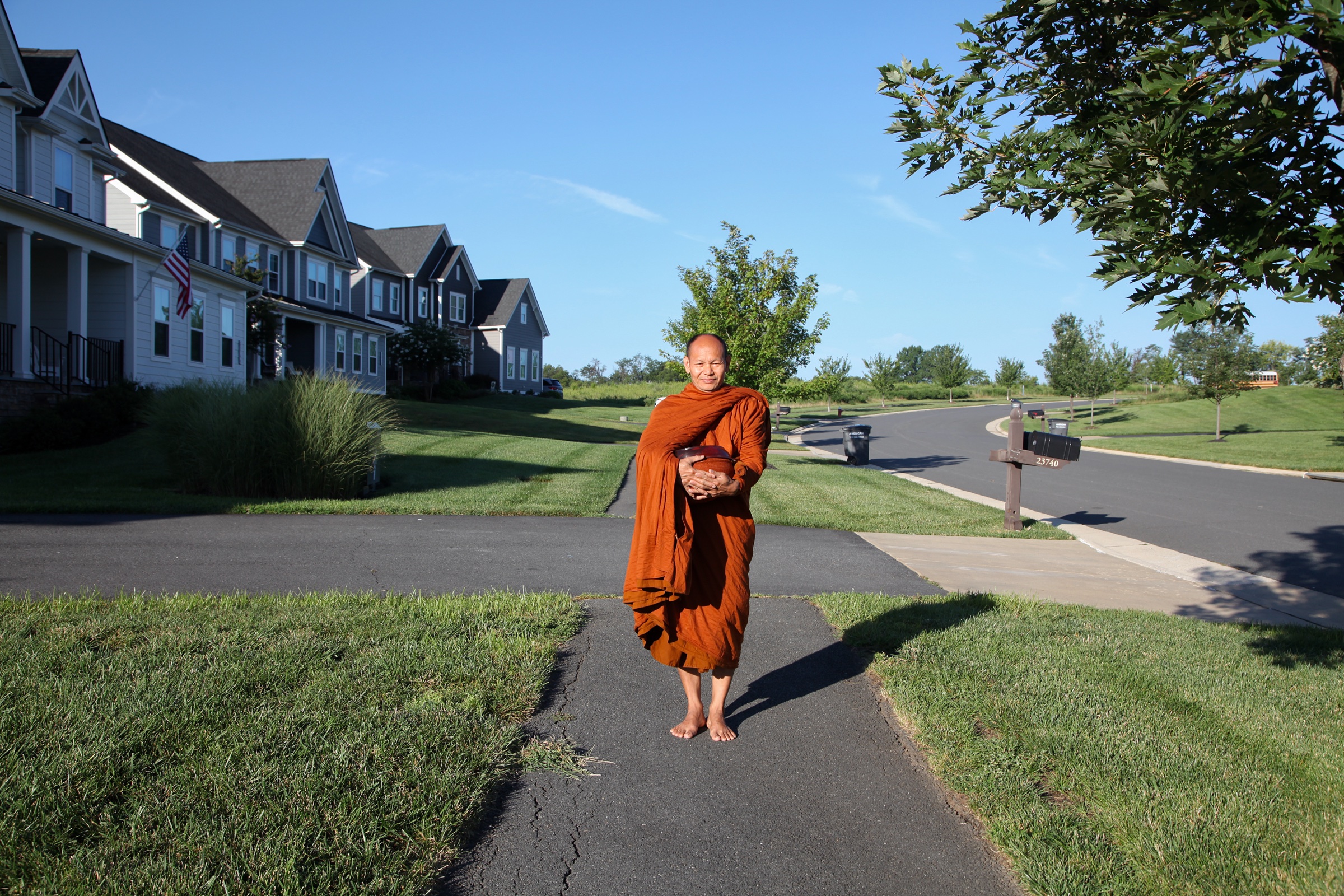 A monk standing barefoot on a suburban driveway in clear morning light