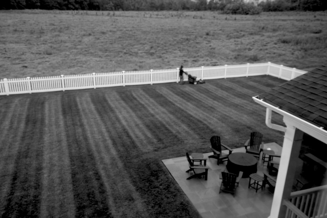 A distant figure pushing a mower across a lawn seen from above