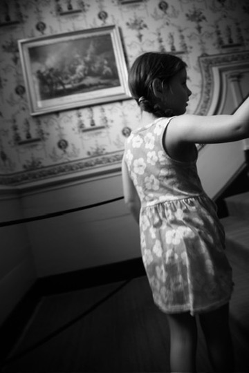 A girl in a patterned dress moving through a room with floral wallpaper