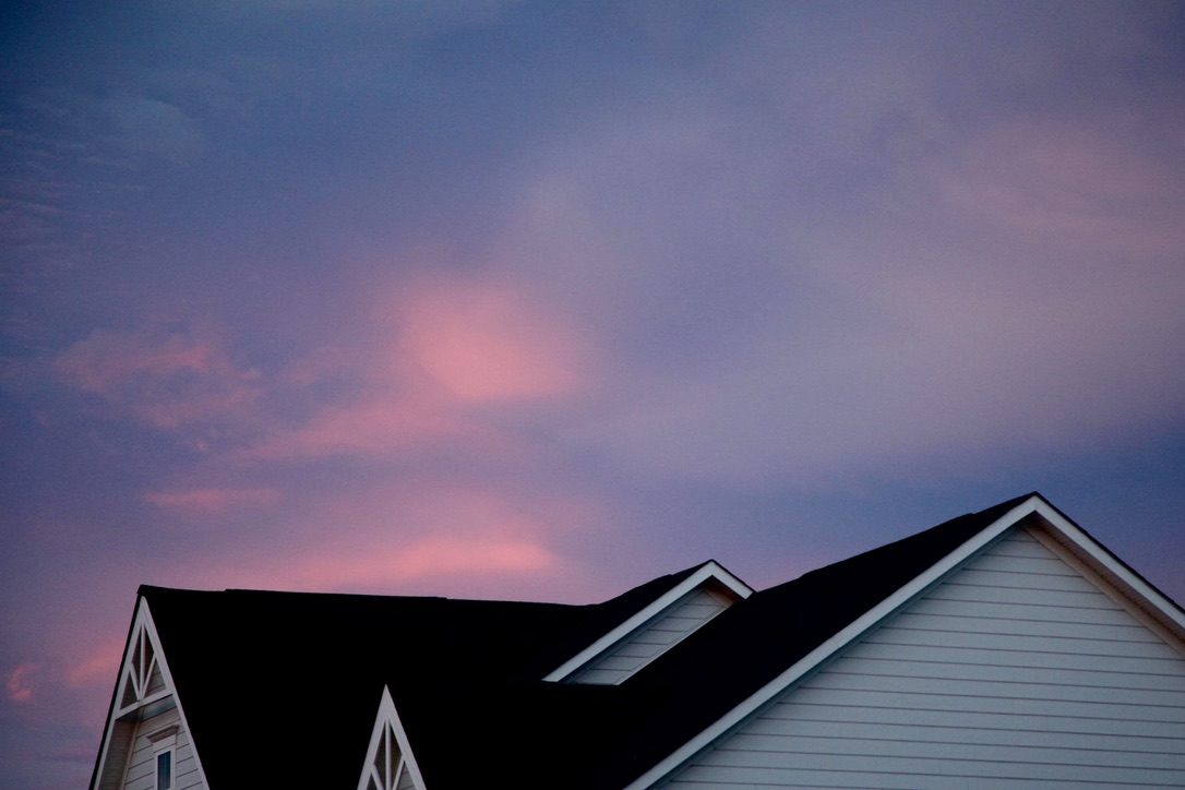 Dark suburban rooflines beneath a pink and blue evening sky