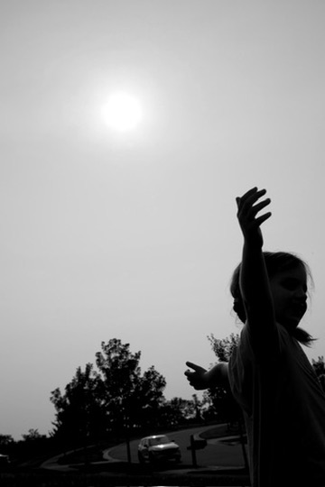 A child silhouetted beneath the sun with one arm raised