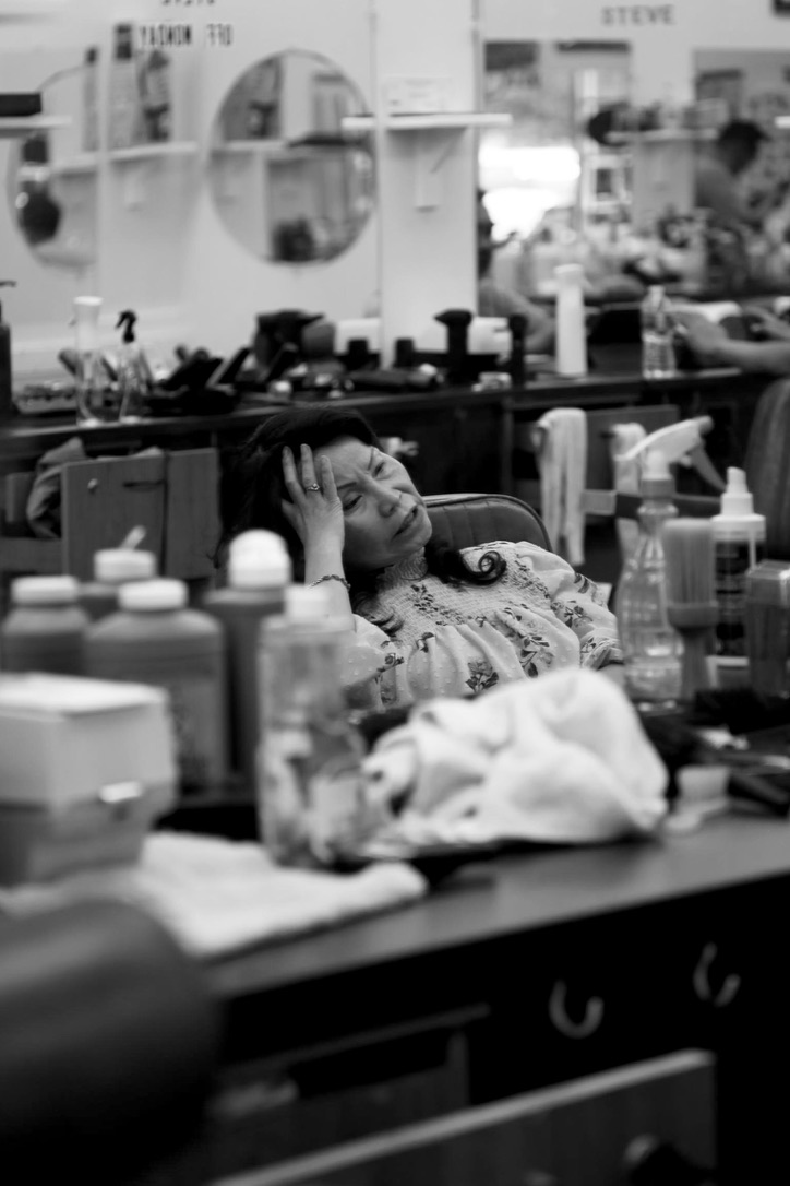 A woman resting with her hand to her forehead in a busy salon