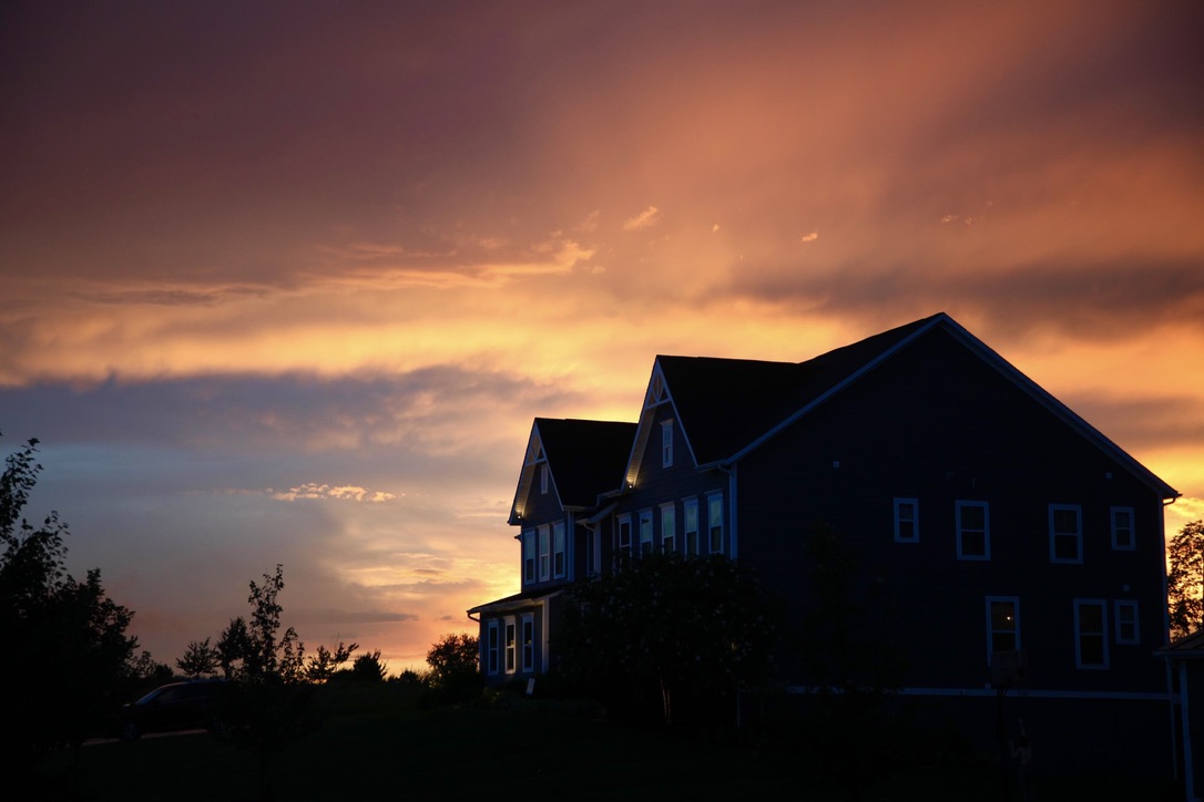 A dark suburban house silhouetted beneath an orange and violet sunset
